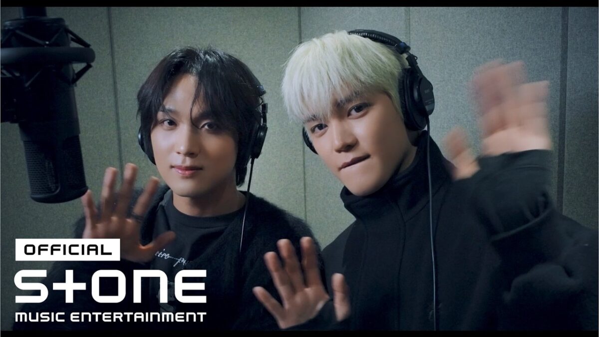 Taeyong e Haechan acenam para a câmera em um estúdio de gravação, usando fones de ouvido.