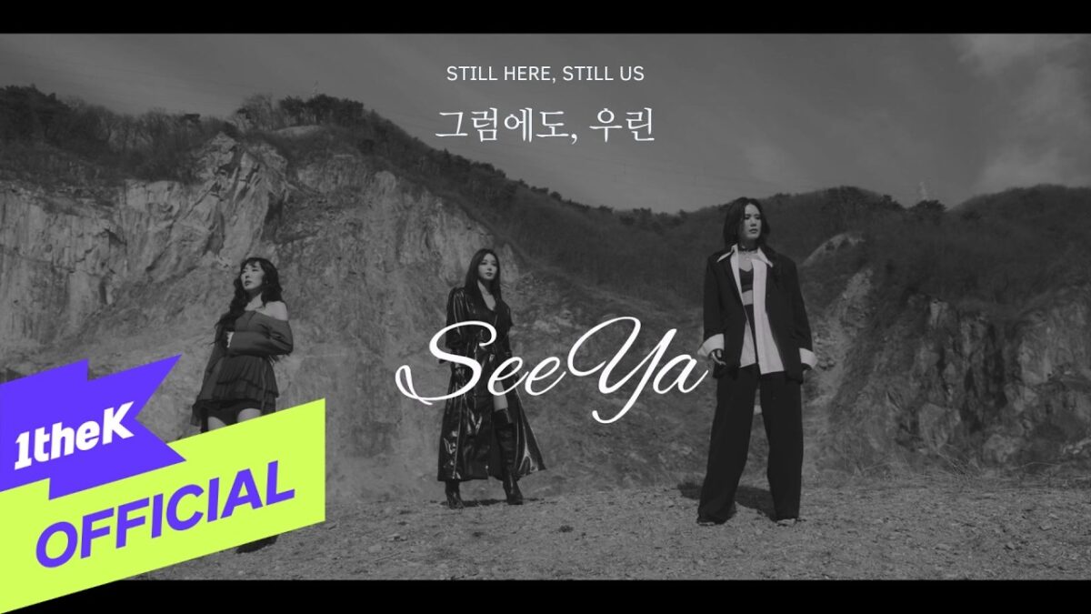 Três mulheres em trajes estilizados posam em uma paisagem montanhosa, com o título "Still Here, Still Us" em destaque.