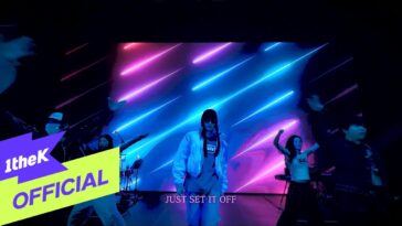 Artistas dançam em palco iluminado por luzes neon, com a frase "JUST SET IT OFF" em destaque.