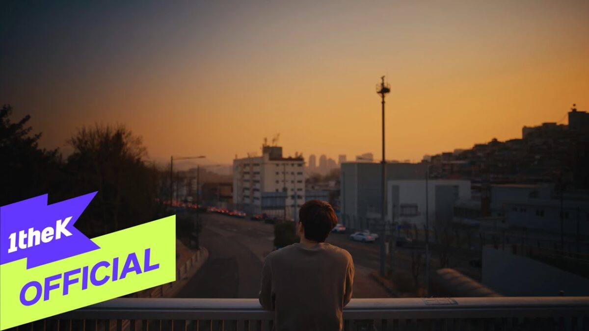 Um homem observa o pôr do sol sobre a cidade, refletindo em um cenário urbano tranquilo.