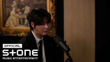 Jungsuk canta em um estúdio elegante, com um microfone à sua frente e uma pintura clássica ao fundo.
