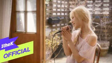 Cantora com cabelo platinado segura microfone enquanto canta em ambiente iluminado e aconchegante.