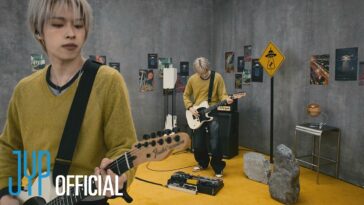 Músico com guitarra elétrica toca ao vivo em um cenário decorado com pôsteres e objetos criativos.
