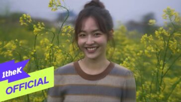 Jovem sorridente em um campo de flores amarelas, com um suéter listrado, transmitindo alegria e leveza.