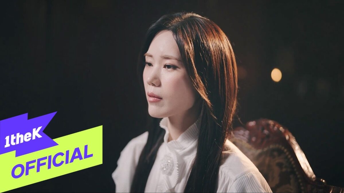 Kim Yeon Ji com expressão contemplativa, vestindo uma blusa branca, em um ambiente com luz suave e fundo escuro.