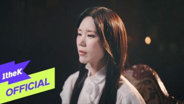 Kim Yeon Ji com expressão contemplativa, vestindo uma blusa branca, em um ambiente com luz suave e fundo escuro.