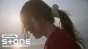 Jovem com cabelo preso, usando blusa vermelha, contemplando o horizonte sob luz suave ao pôr do sol.