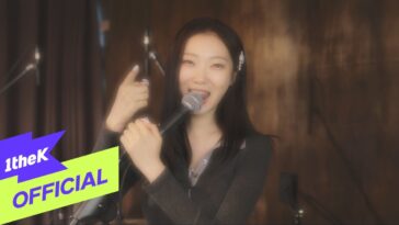 Sohlhee canta animada com microfone em mãos, sorrindo para a câmera em um cenário musical.