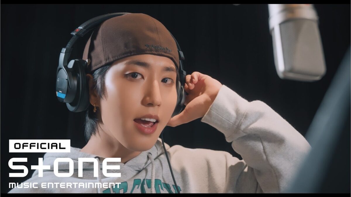 HAN, do Stray Kids, está em estúdio usando fones de ouvido e sorrindo enquanto grava uma música.