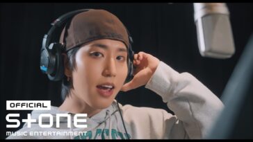 HAN, do Stray Kids, está em estúdio usando fones de ouvido e sorrindo enquanto grava uma música.