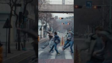 Grupo de pessoas atravessando uma rua em movimento, com semáforo vermelho ao fundo e árvores sem folhas nas laterais.