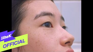 Close-up do rosto de uma jovem com pele levemente brilhante, olhando para o lado em um ambiente iluminado.