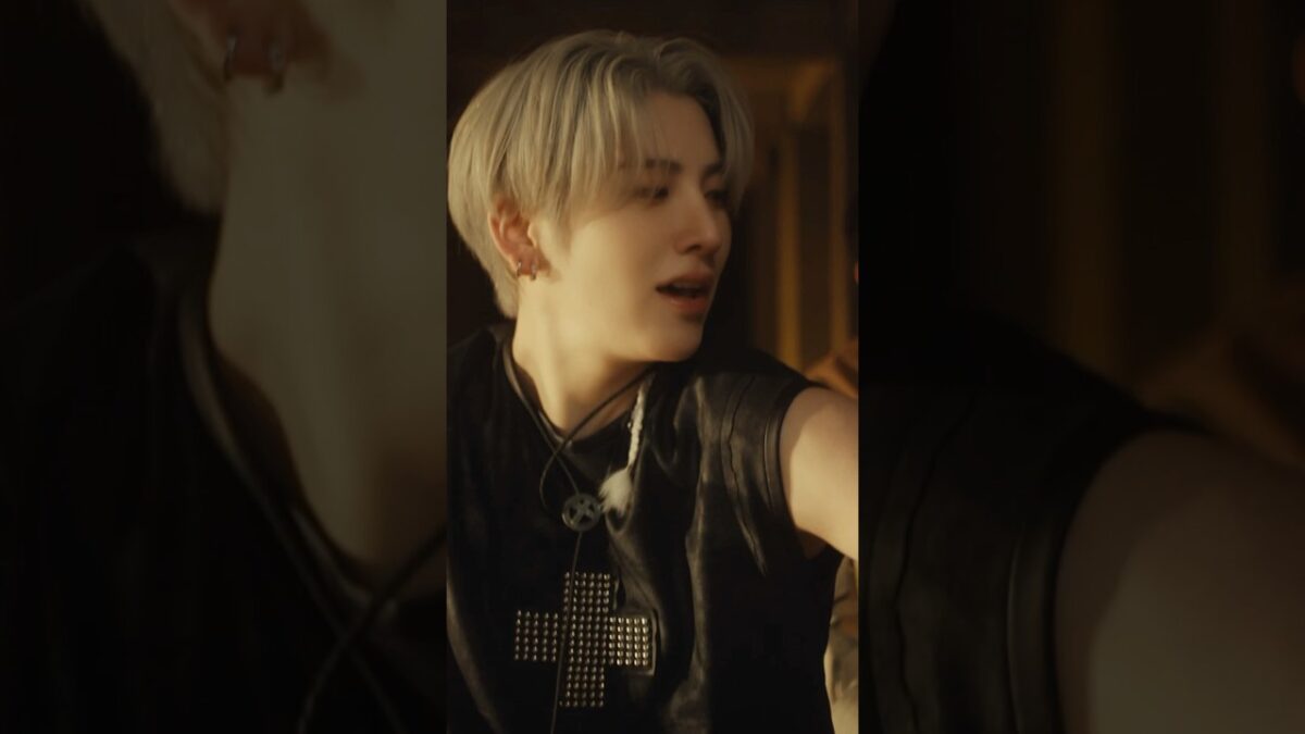 Jovem com cabelo platinado e camisa preta, expressando emoção durante a performance do grupo