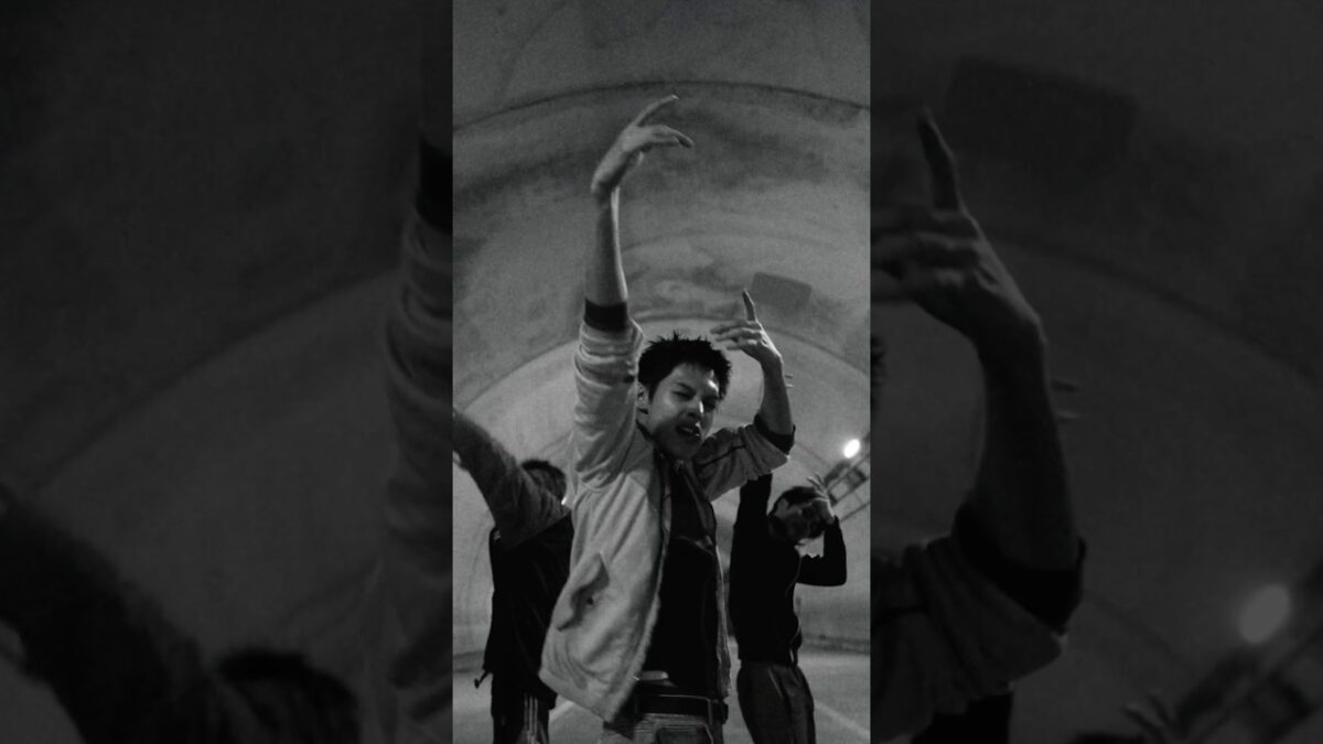 Dançarino em movimento expressivo sob iluminação suave, com outros dançarinos ao fundo em uma performance conceitual.