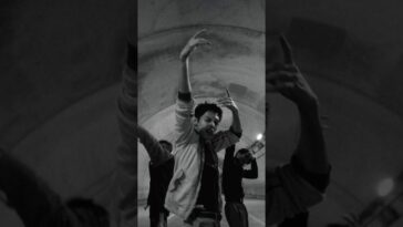 Dançarino em movimento expressivo sob iluminação suave, com outros dançarinos ao fundo em uma performance conceitual.