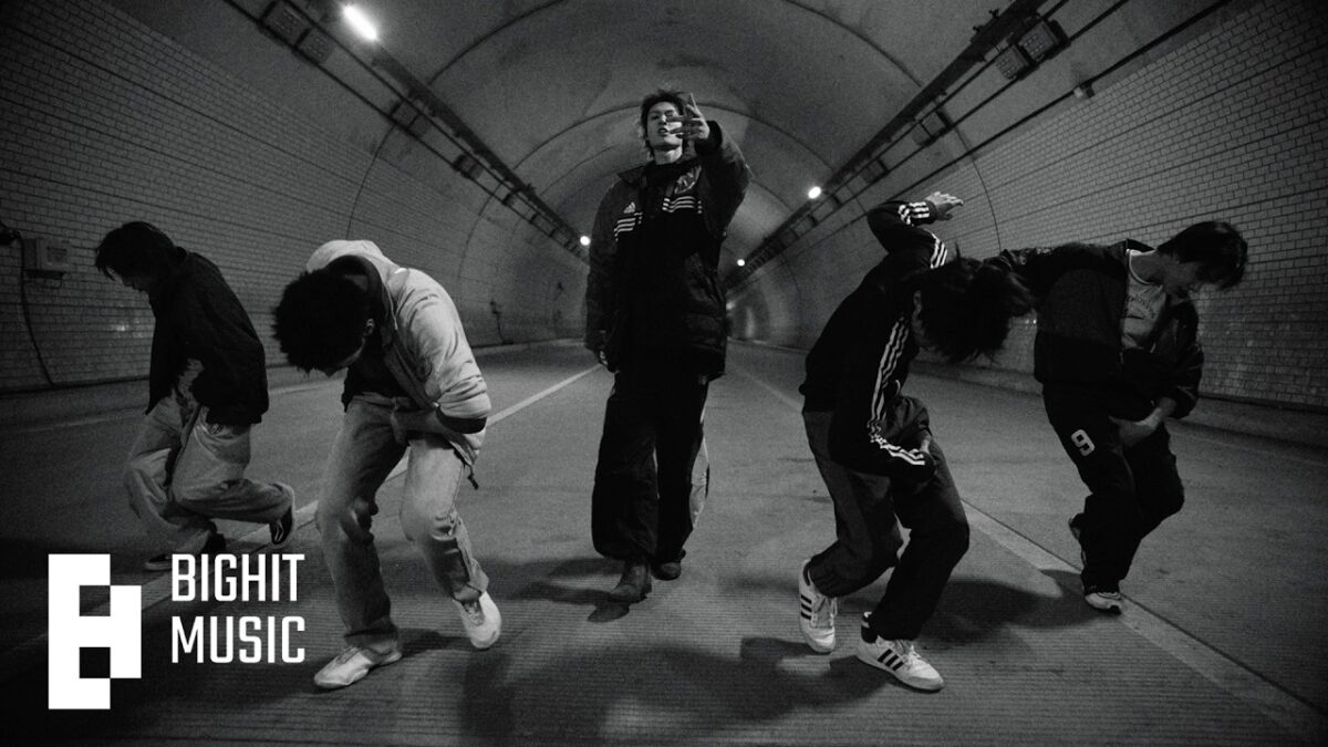 Grupo de dançarinos performando em um túnel, com destaque para um dançarino central em pose dinâmica.