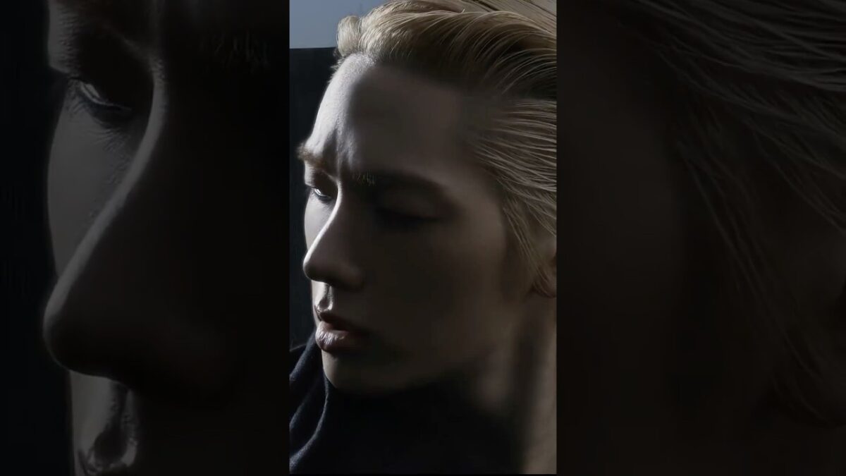 Close-up de um jovem com cabelo loiro, expressão intensa, em um fundo escuro e iluminado de forma dramática.