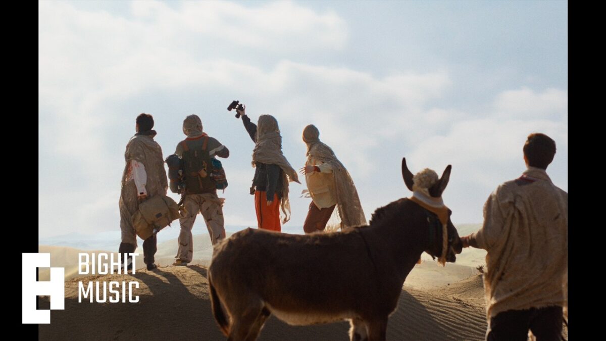 Quatro pessoas em vestimentas tradicionais observam o horizonte em um deserto, acompanhados por um burro.