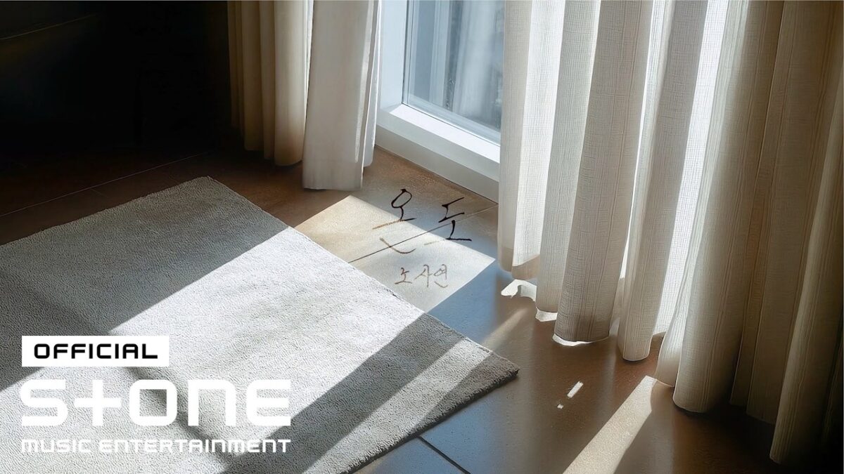Um tapete claro sobre um piso de madeira, com luz natural entrando por cortinas brancas.