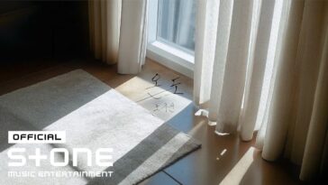 Um tapete claro sobre um piso de madeira, com luz natural entrando por cortinas brancas.