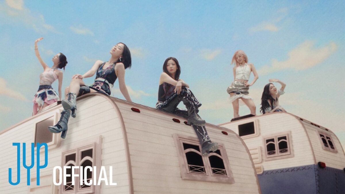 Cinco integrantes do ITZY dançam e se divertem em cima de trailers sob um céu azul claro.