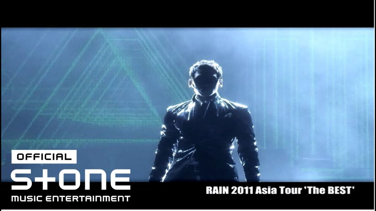 Rain em performance dramática, iluminado por luzes de palco e efeitos visuais.