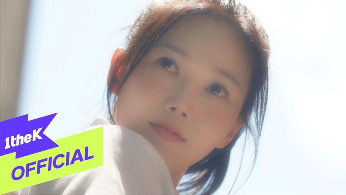Hyojung, do OH MY GIRL, olhando suavemente para o horizonte em um cenário iluminado.
