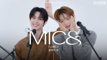 Dois cantores sorrindo em um palco, um deles com as mãos no rosto, prontos para se apresentar ao vivo.