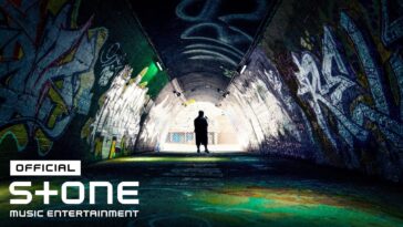 Homem em pé em um túnel grafitado, iluminado por luzes artificiais, criando um ambiente urbano e enigmático.
