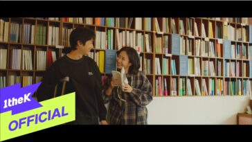 Yun Seong e uma jovem sorridente em uma biblioteca, trocando olhares enquanto seguram um livro juntos.
