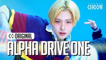 Jovem com cabelo loiro e expressão intensa dança em fundo azul, com texto "ALPHA DRIVE ONE" em destaque.