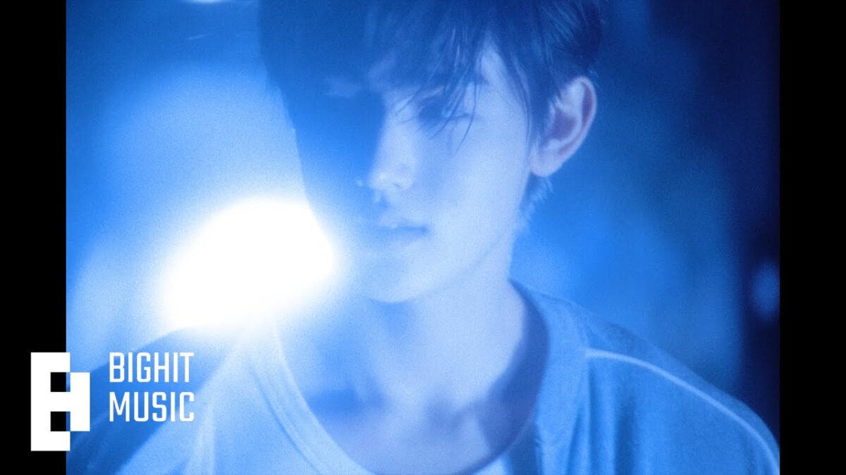 Um jovem com lábios azuis e expressão introspectiva, iluminado por uma luz suave e azul.