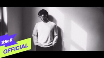 Sung Si Kyung, com óculos, posa de forma contemplativa contra uma parede iluminada.