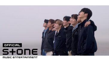 Sete membros do grupo Wanna One posam juntos, sorrindo e olhando para o horizonte em um ambiente nebuloso.