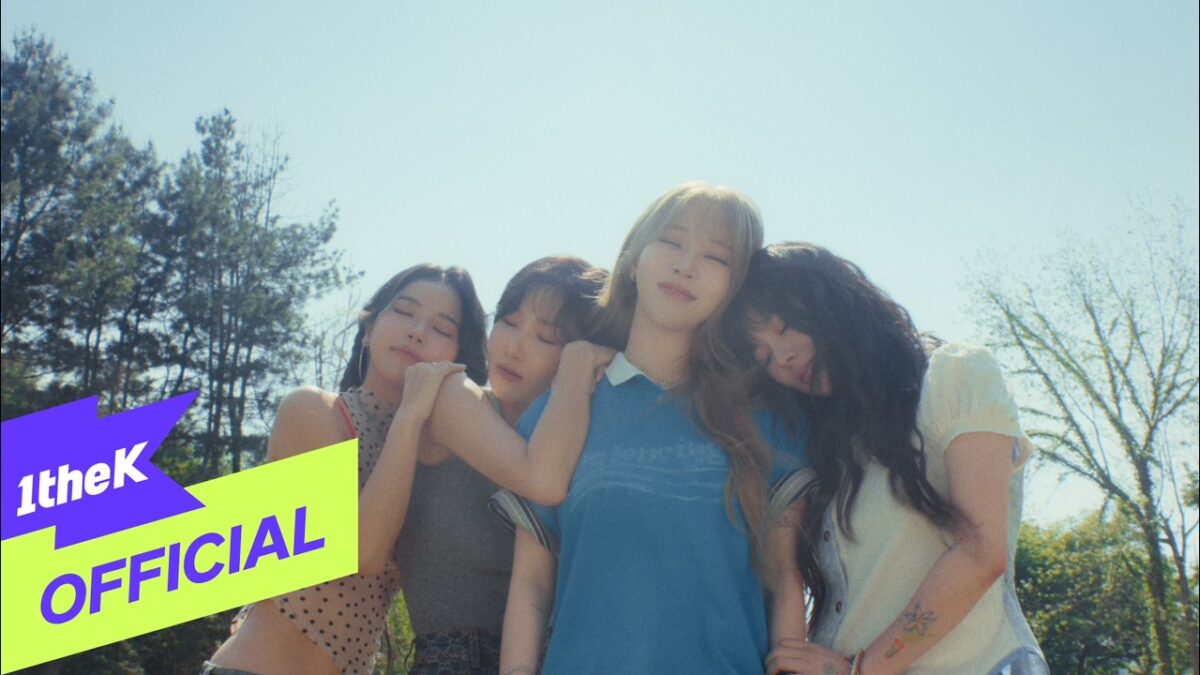 Quatro integrantes da MAMAMOO se abraçam sob um céu azul, transmitindo uma sensação de amizade e emoção.