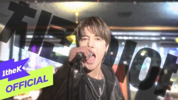 Kim Hyun Joong canta empolgado com microfone em mãos, em um cenário vibrante e iluminado.