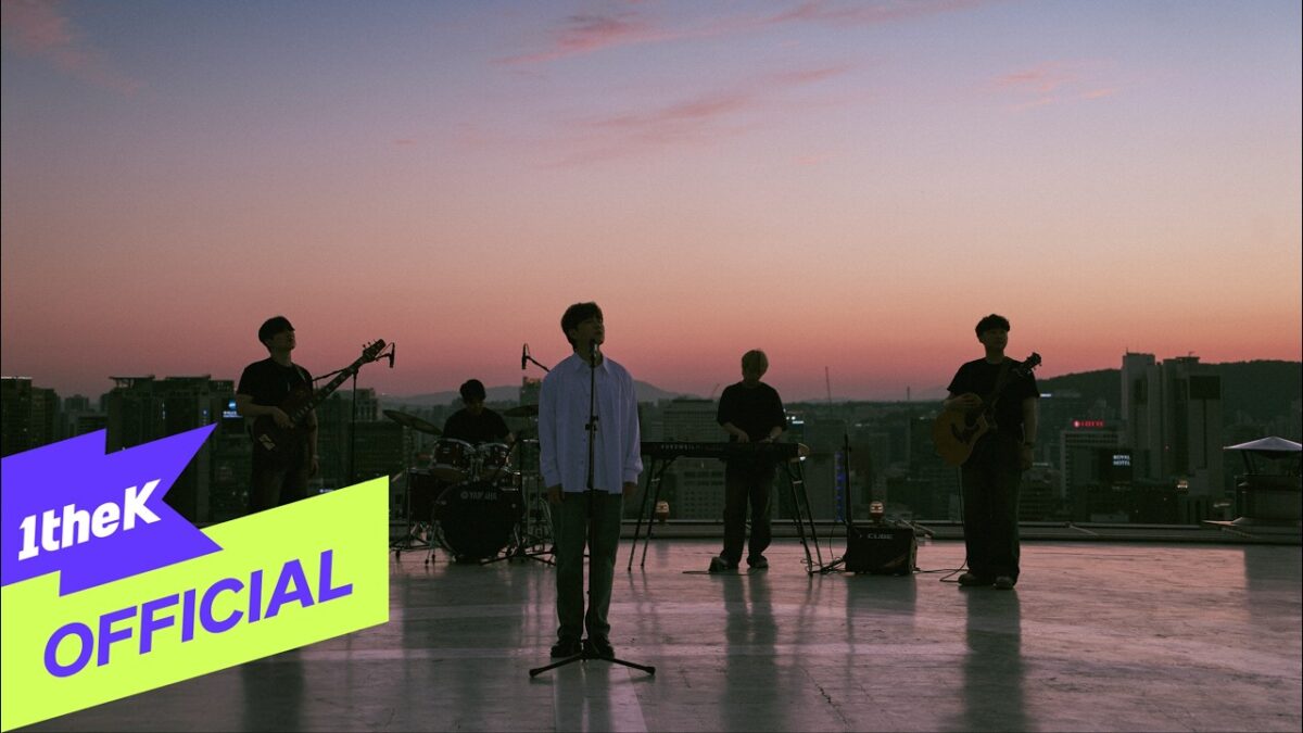 Banda se apresenta ao pôr do sol em um telhado, com instrumentos e microfone em destaque.