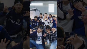 Grupo de jovens dançarinos em poses dinâmicas, usando roupas esportivas e bandanas, em ambiente interno iluminado.