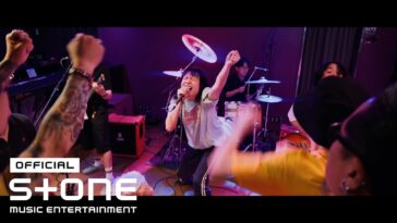 Vocalista performa energicamente no palco, cercado por fãs animados e músicos, durante gravação do clipe "Little Baby".