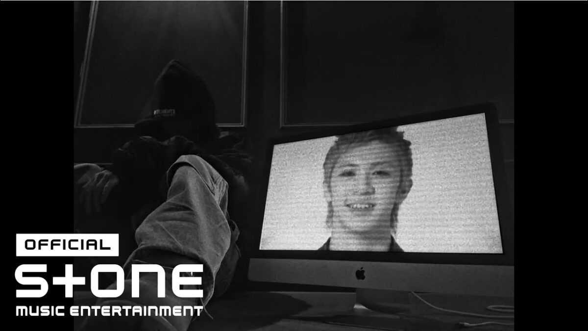 Um jovem sentado em um ambiente escuro, com um computador exibindo uma imagem em preto e branco de um rosto sorridente.