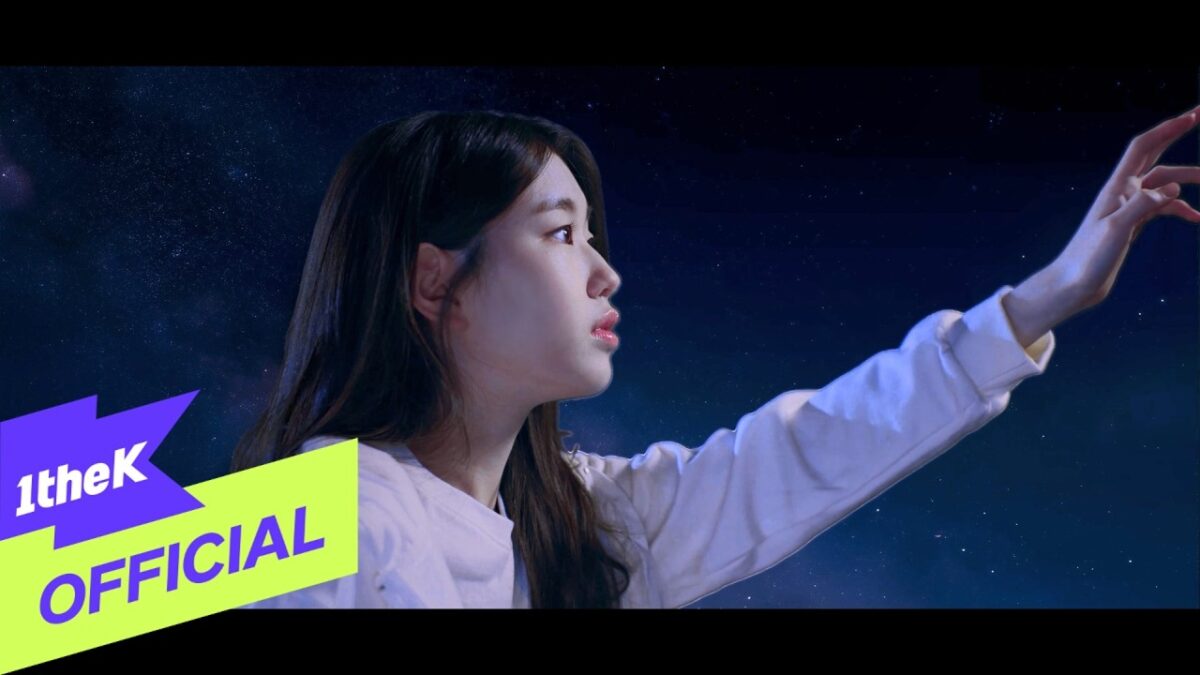 Jovem com expressão sonhadora estende a mão em direção a um céu estrelado no clipe "Glowing".