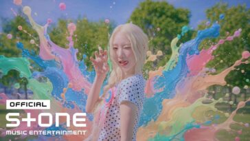 YEOJIN sorri e pisca, rodeada por explosões coloridas de tinta em um cenário ensolarado.
