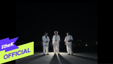 Três artistas vestidos de branco em um cenário noturno, iluminados por luzes da cidade ao fundo.