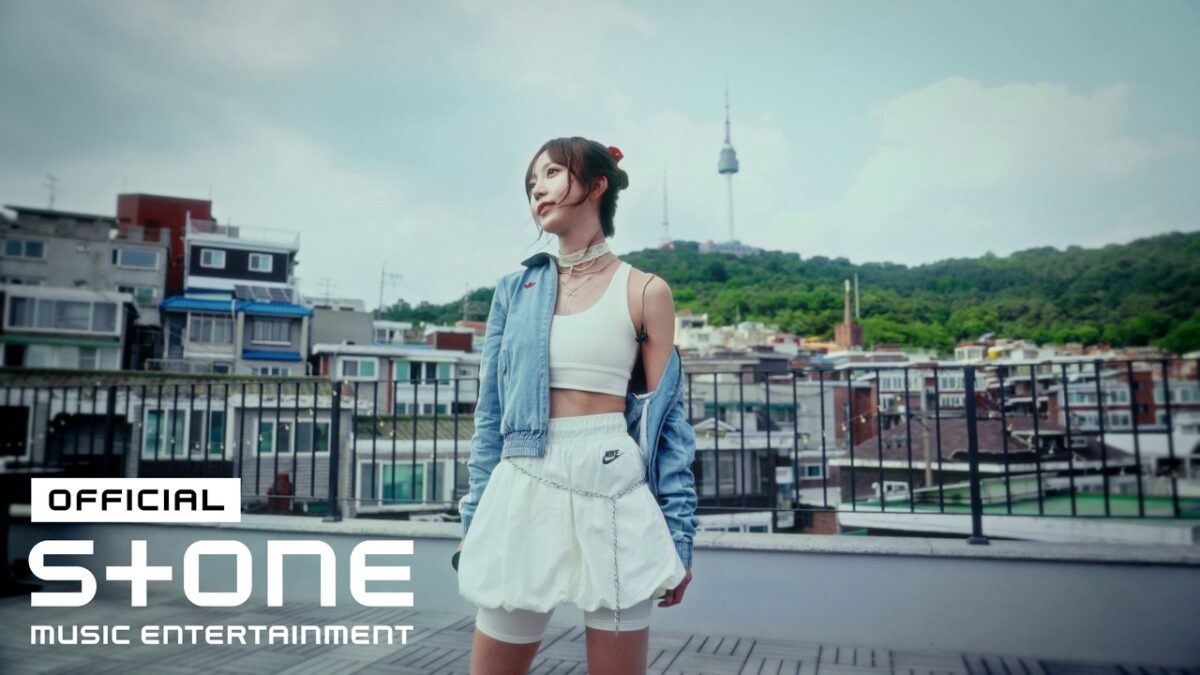 Kim Sohee posa com um look urbano em um terraço, com a Torre Namsan ao fundo.