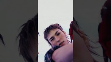 Um jovem com cabelo curto e despojado faz um gesto de piscar enquanto olha para a câmera.