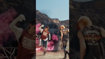THE8 e Vernon dançam em um cenário árido, com fumaça rosa ao fundo, usando roupas casuais e descontraídas.