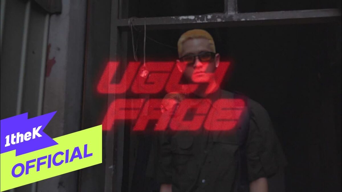 Um jovem com cabelo loiro platinado e óculos escuros, posando em um ambiente urbano com a frase "UGLY FACE" em destaque.