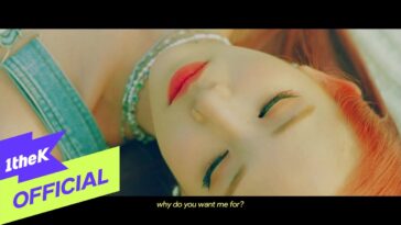 JISSELLE com cabelo laranja, deitada com os olhos fechados, em um clipe musical vibrante e expressivo.