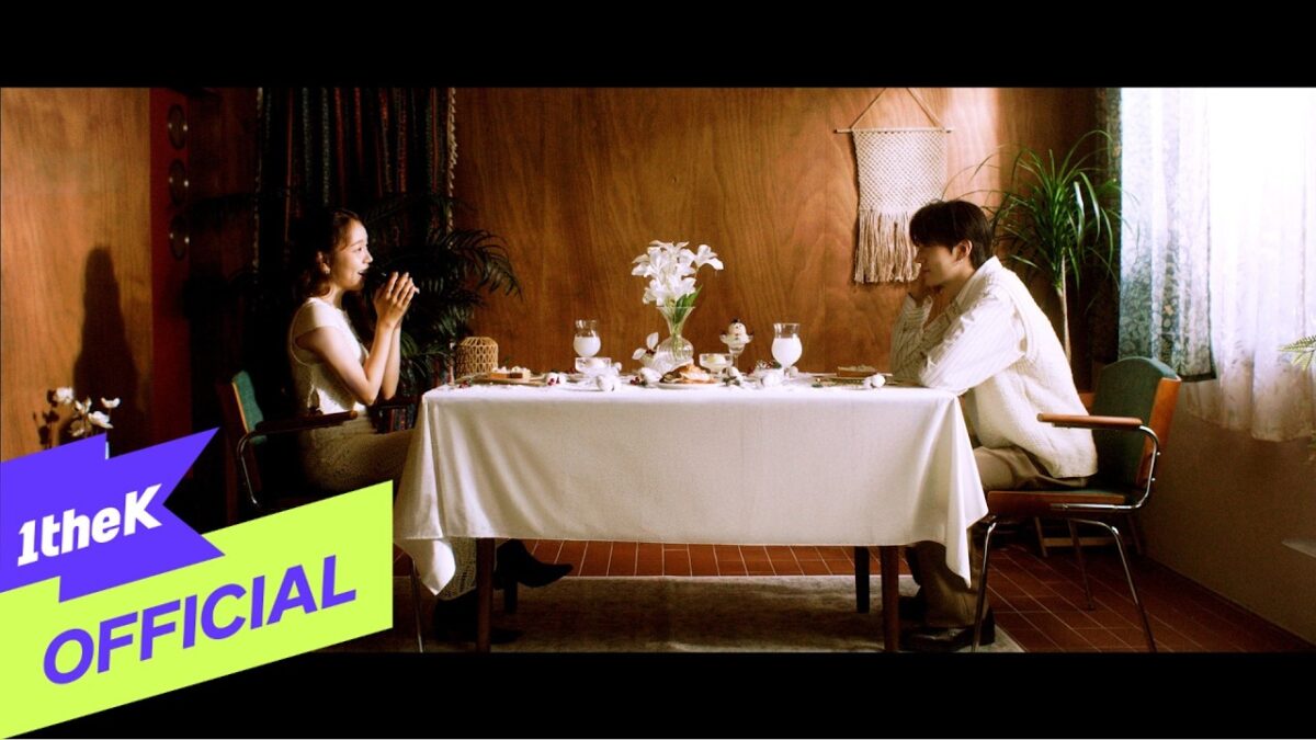 Baek A Yeon e Hyunbin sentados à mesa, conversando em um ambiente aconchegante decorado com flores e luz suave.
