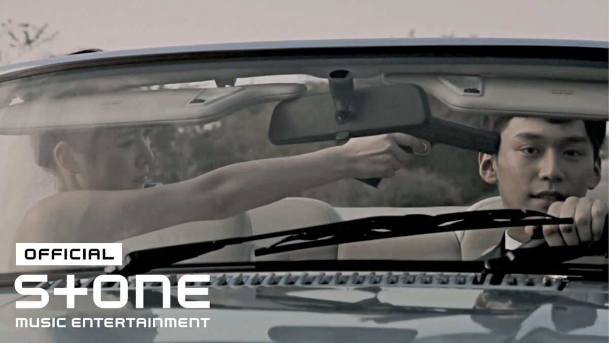 Uma mulher aponta uma arma para um homem dentro de um carro conversível.